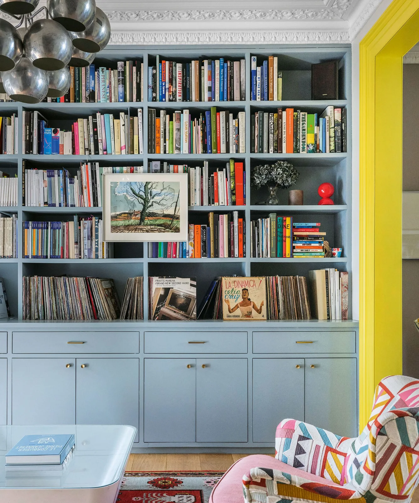 Blue built-in cupboards and drawers support open shelves packed with books and records, with a framed picture across the center.