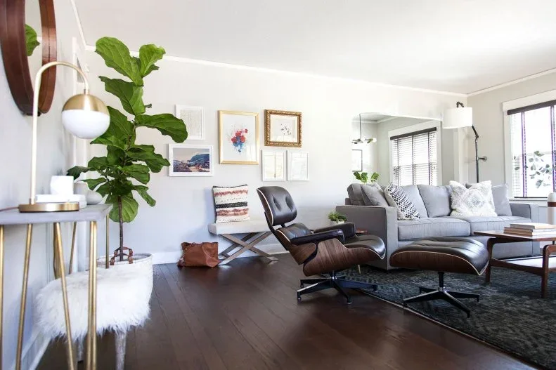 Black lounge chair and ottoman beside a gray sofa, leafy plant and loosely arranged framed pictures.