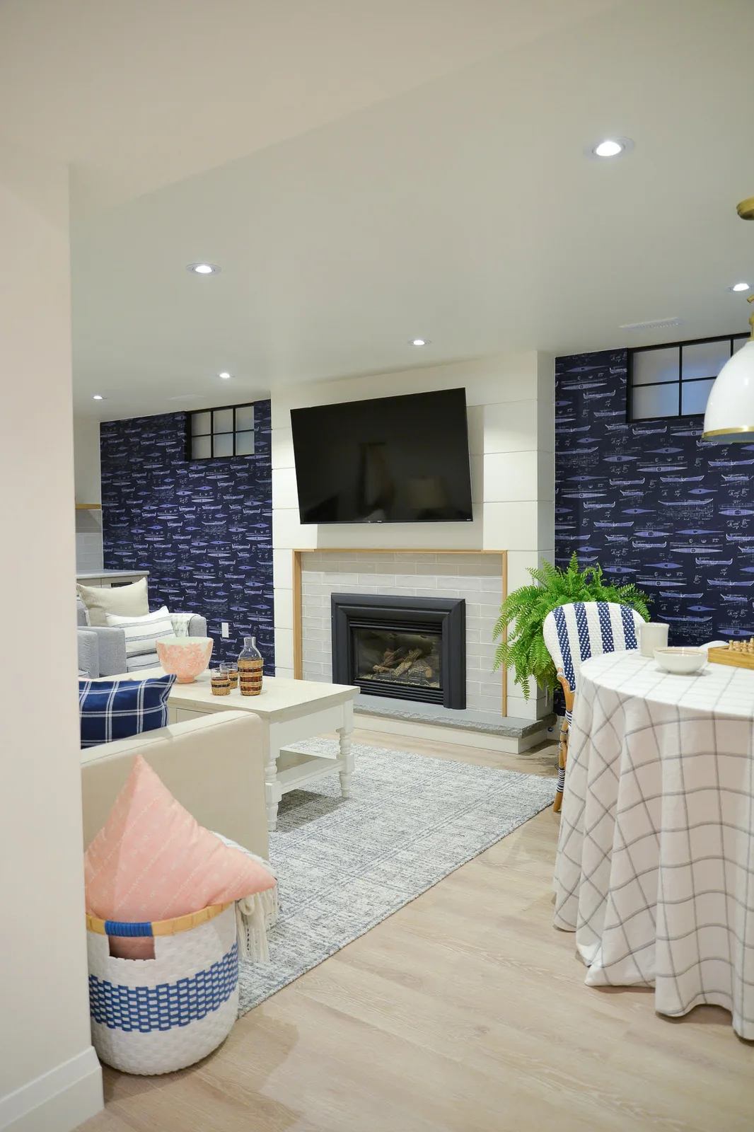 A white shiplap fireplace and television sit between dark blue patterned walls, with pale tile around the insert, a slim wood trim and light seating.