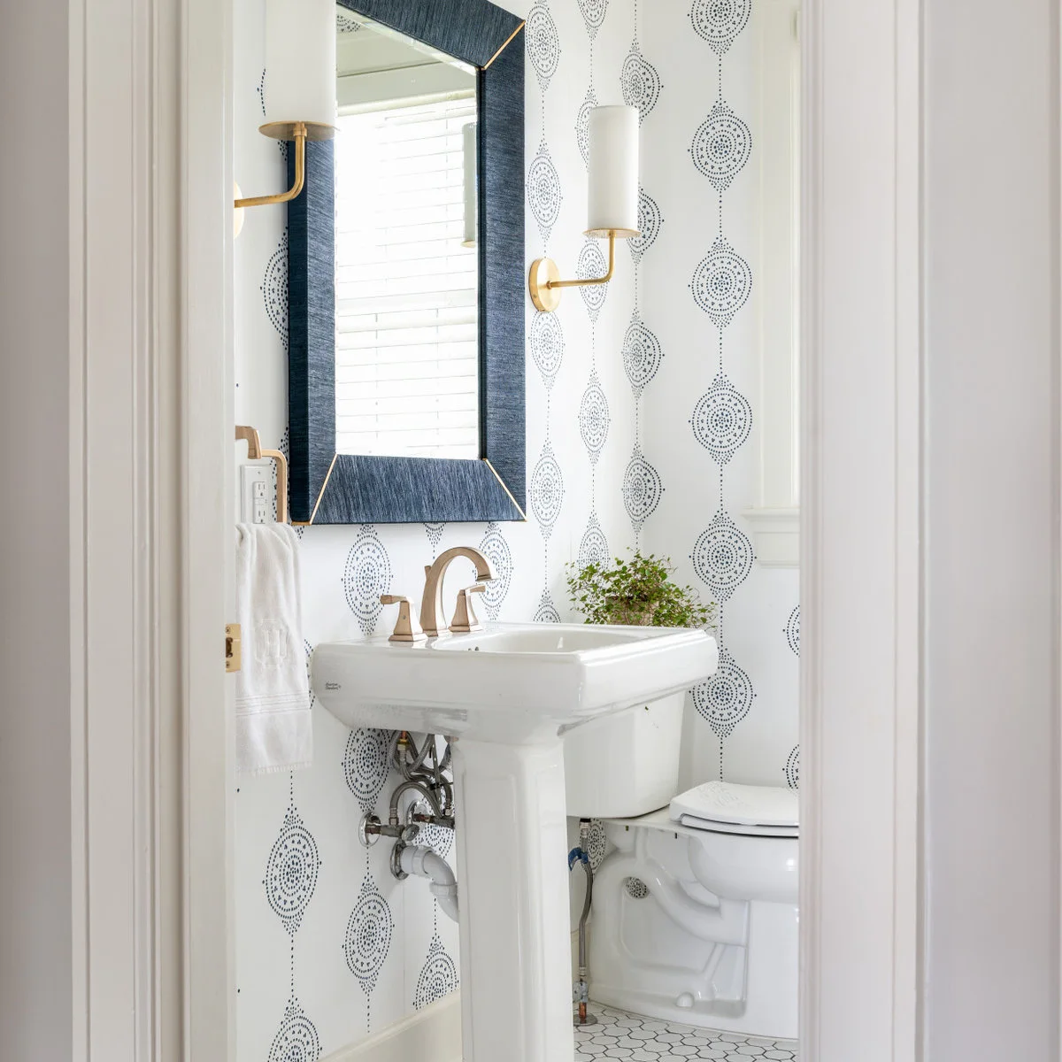A white pedestal sink beneath a blue-framed mirror and paired sconces against dotted patterned walls.