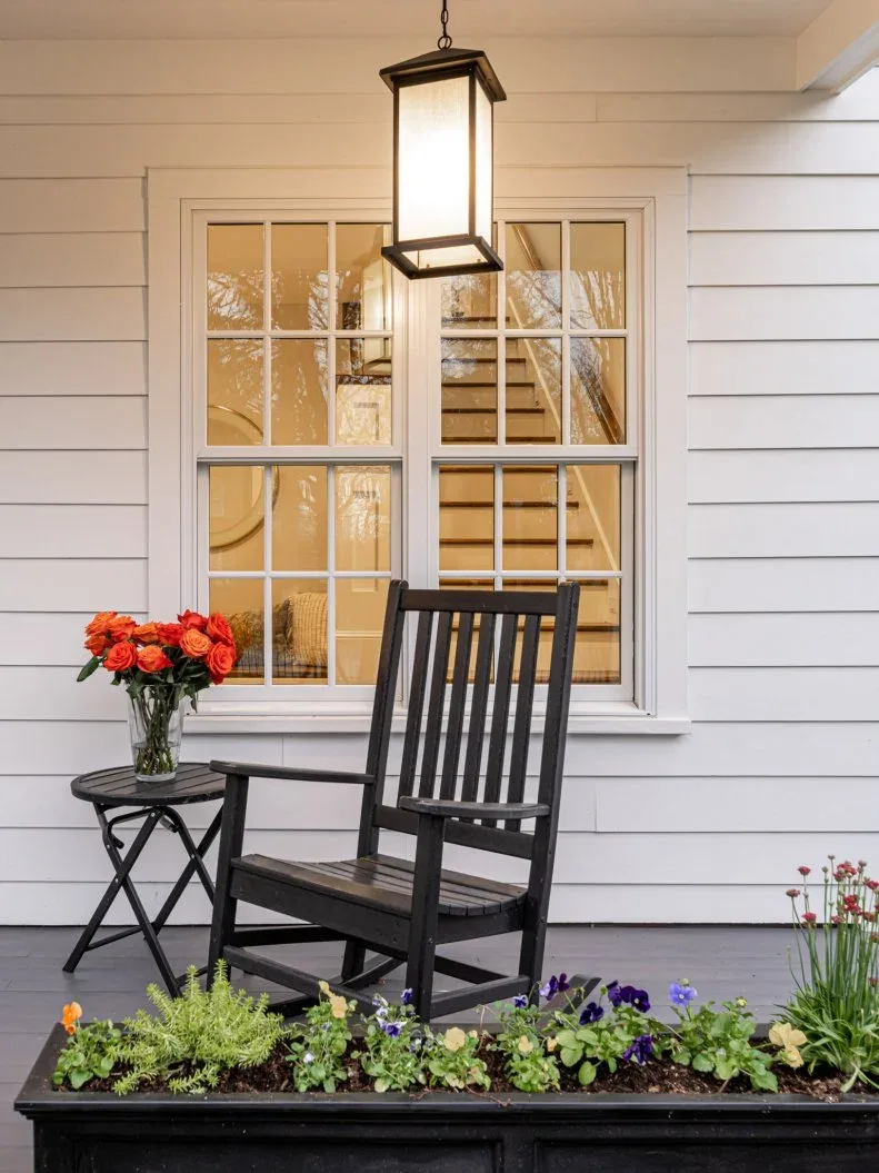 Dark wood rocking chair and small round table on white-sided porch beneath a hanging lantern