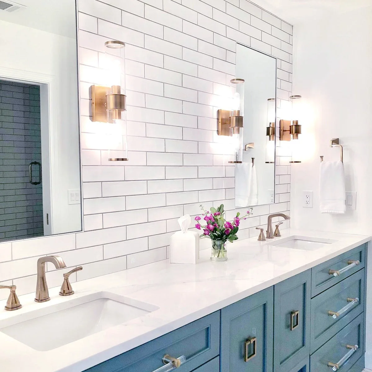 Tall frameless mirrors on white subway tiles above a blue double vanity