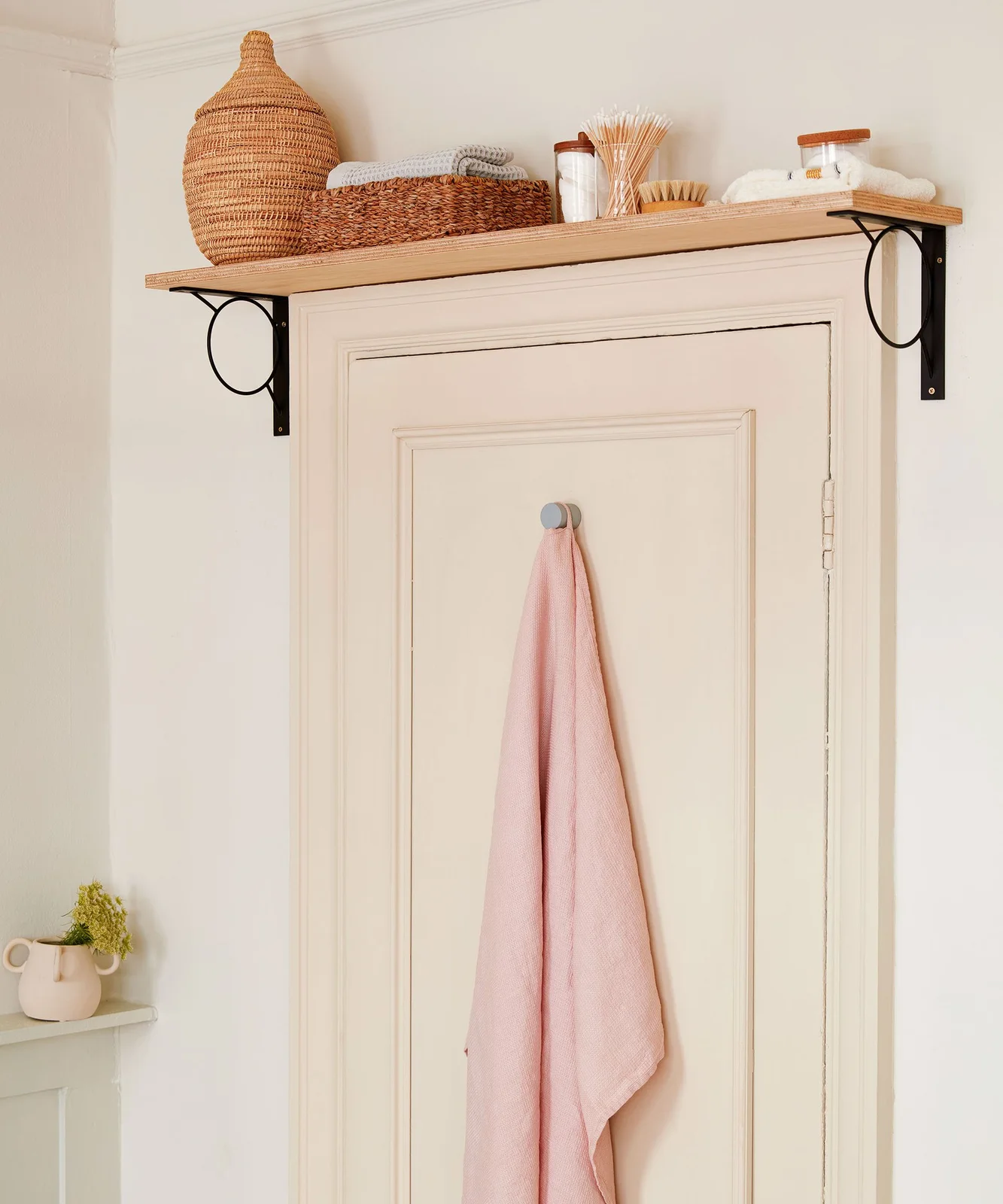 Shelf above a bathroom door holding baskets, towels and jars