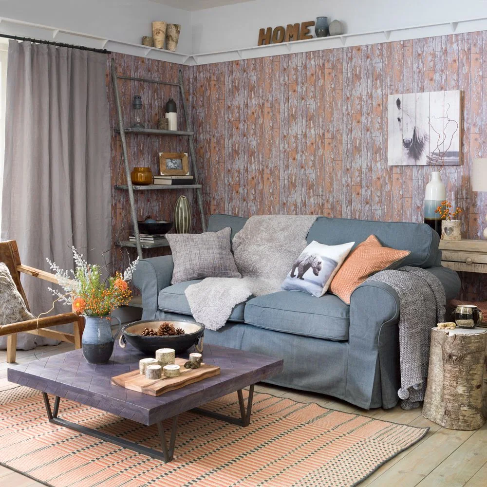 A blue sofa and wood coffee table sit before a faded board-effect wall pattern beside a ladder shelf and plain curtains.