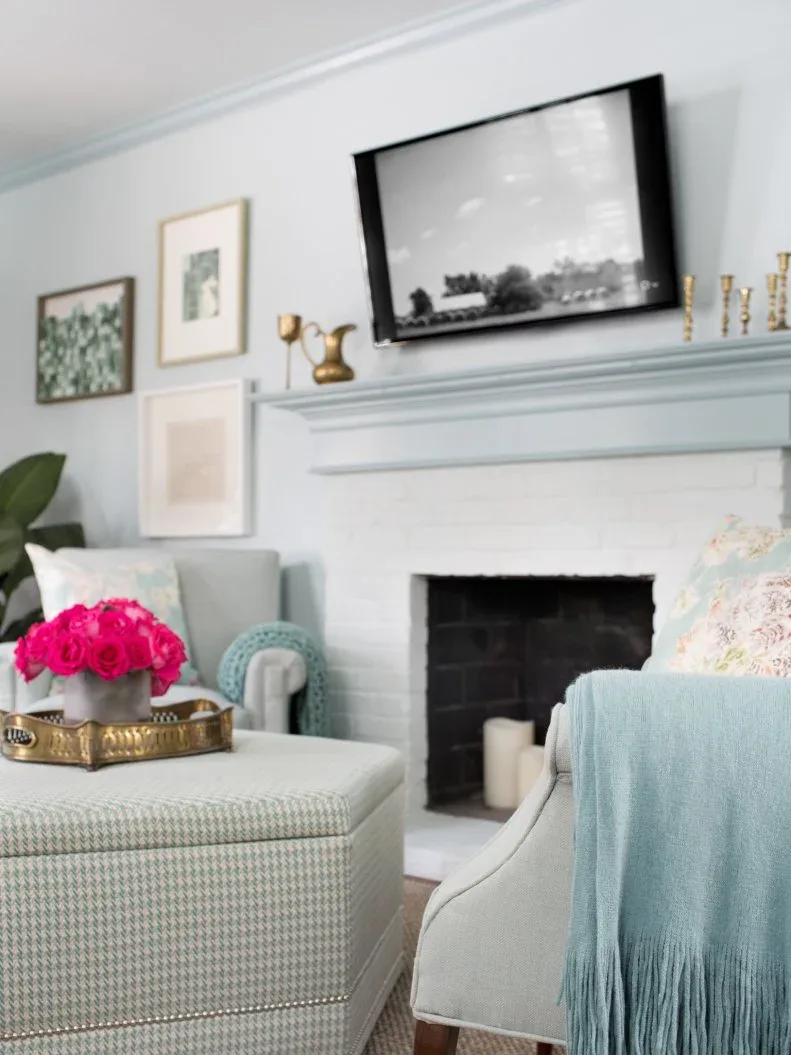 Pale blue mantel beneath wall-mounted television with small gold-toned vessels and candlesticks
