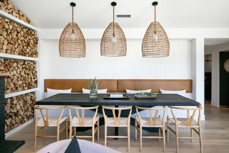 Three woven pendants hang above a dark dining table, pale wood chairs and a brown upholstered wall bench.
