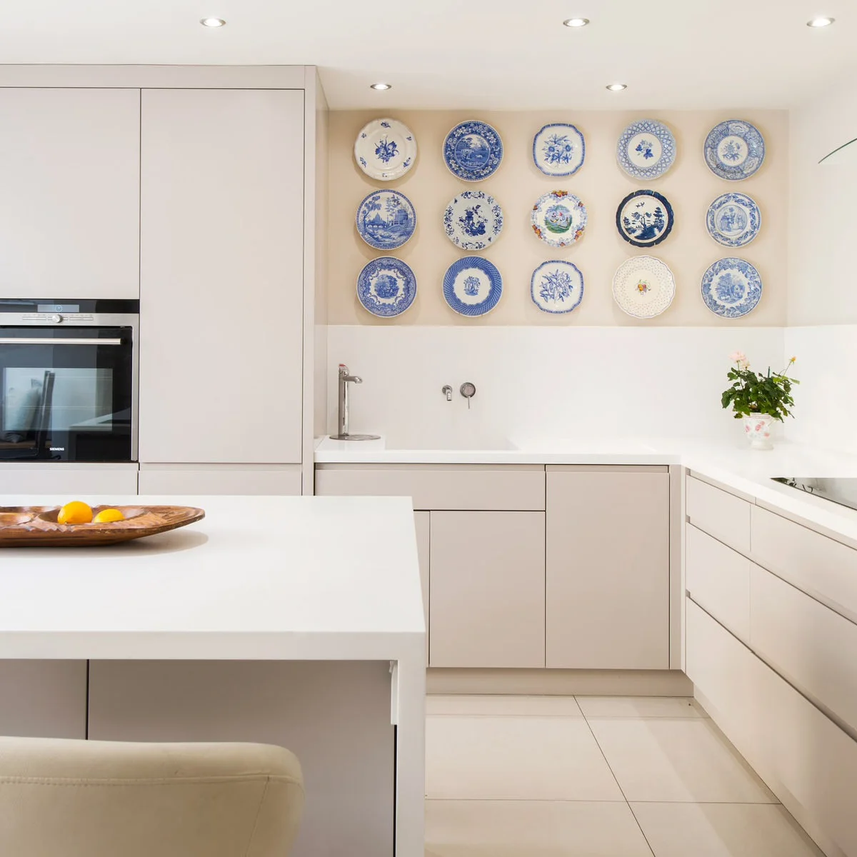 Three rows of blue and white decorative plates above a sink in a pale modern kitchen.