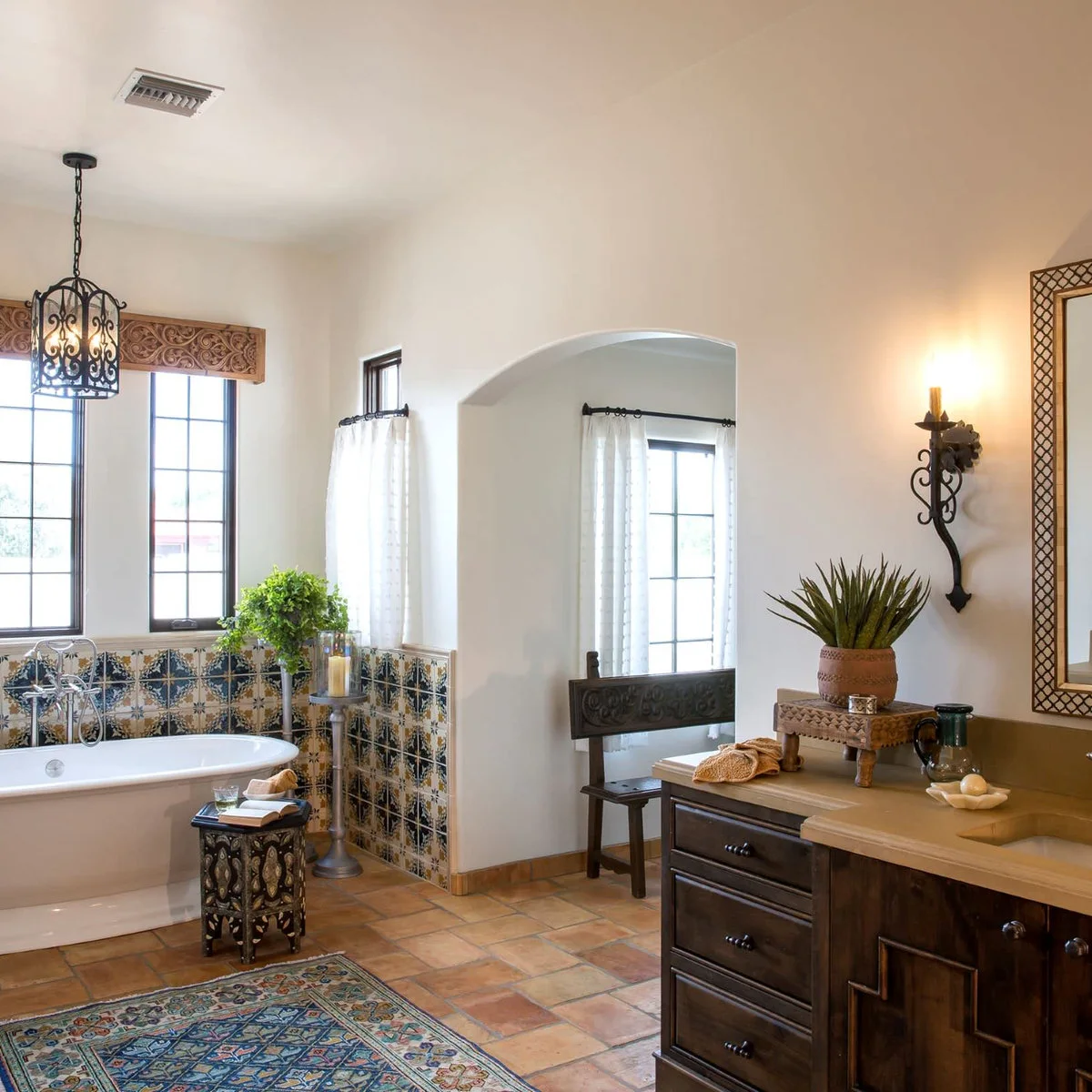 Mediterranean-inspired bathroom with blue-and-ochre wall tiles around a white tub and warm square floor tiles