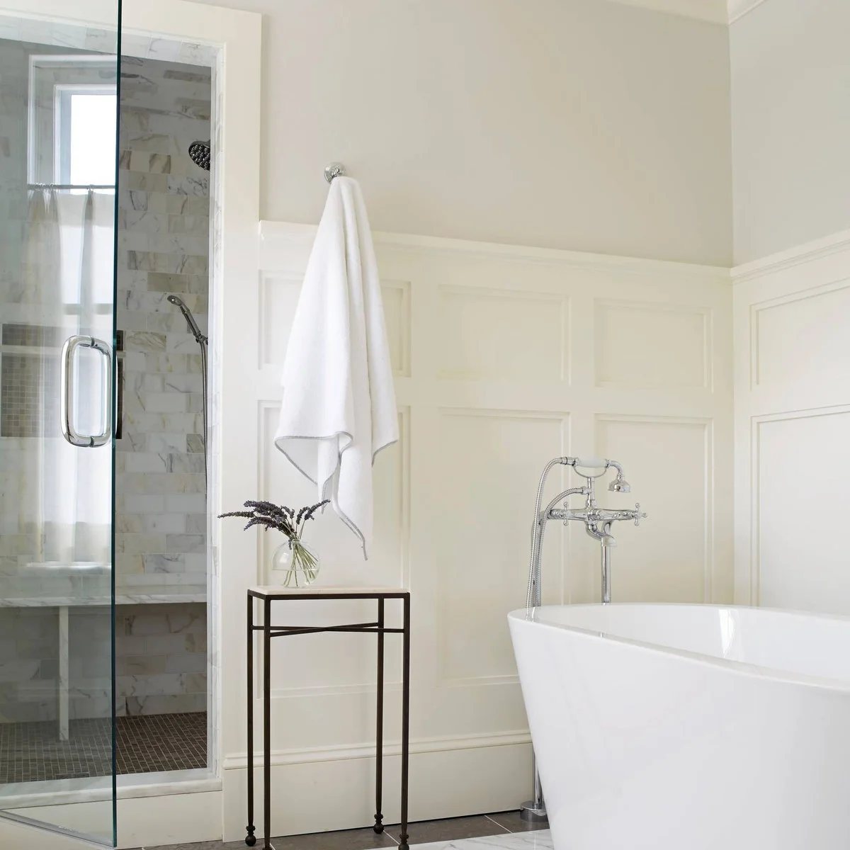 Pale framed bathroom panels outside a glass shower beside a freestanding tub