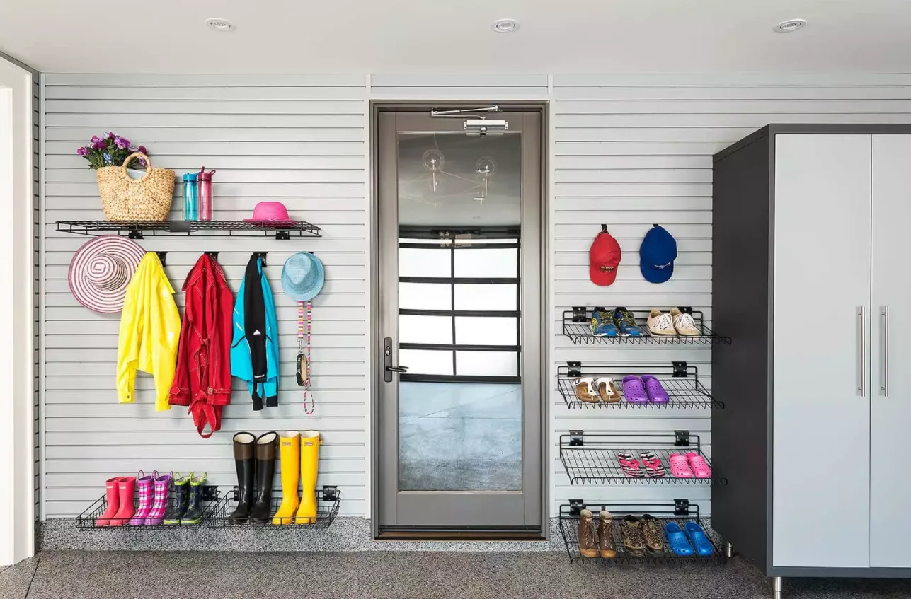 Garage entry with wall-mounted coat hooks, wire shoe baskets, a boot shelf and tall closed storage beside the door