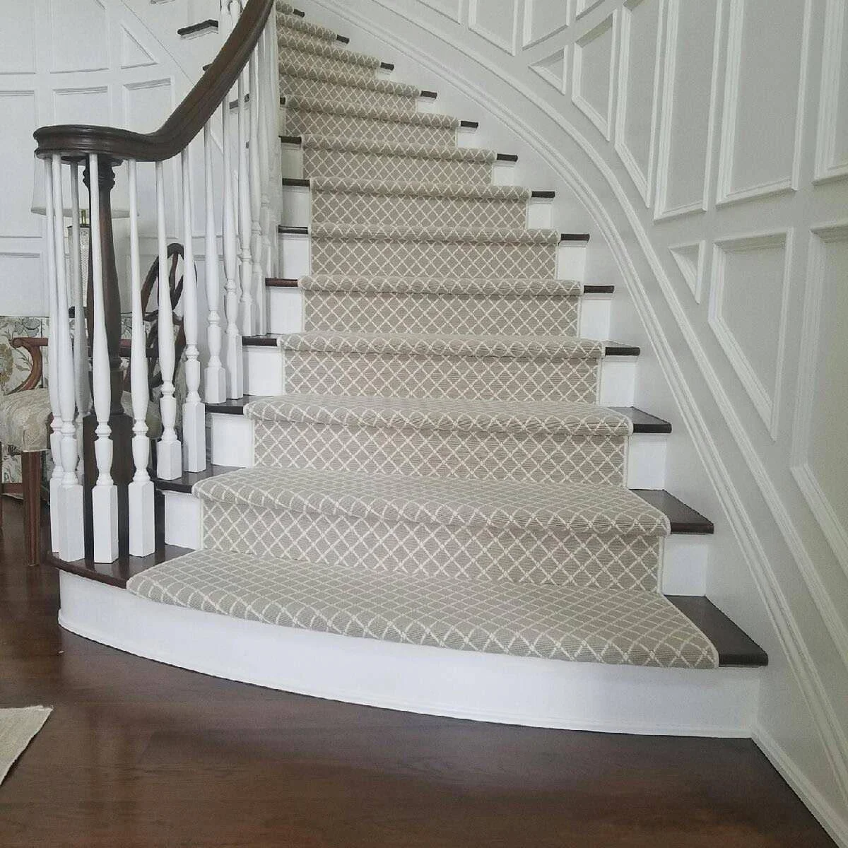 Curved white staircase with a pale diamond-pattern runner and rectangular wall paneling