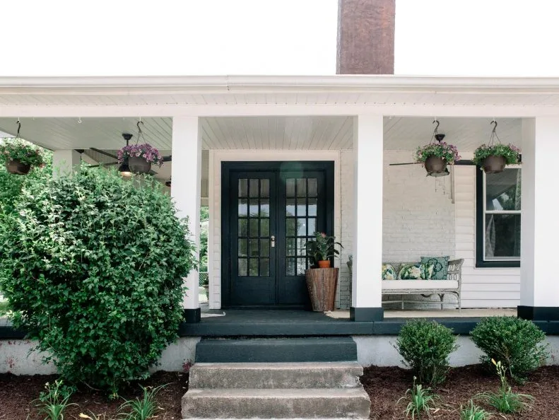 Dark green glazed double doors on white porch with hanging baskets, pale bench and central steps