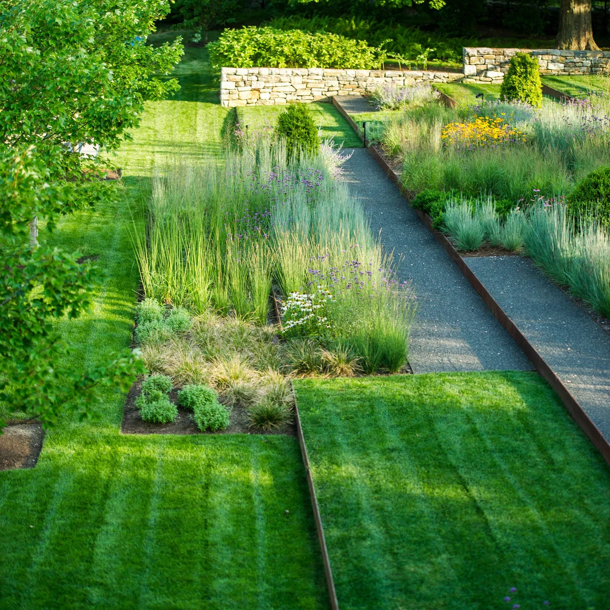 Thin brown metal edges define planted strips, rectangular lawn sections and gray gravel paths.