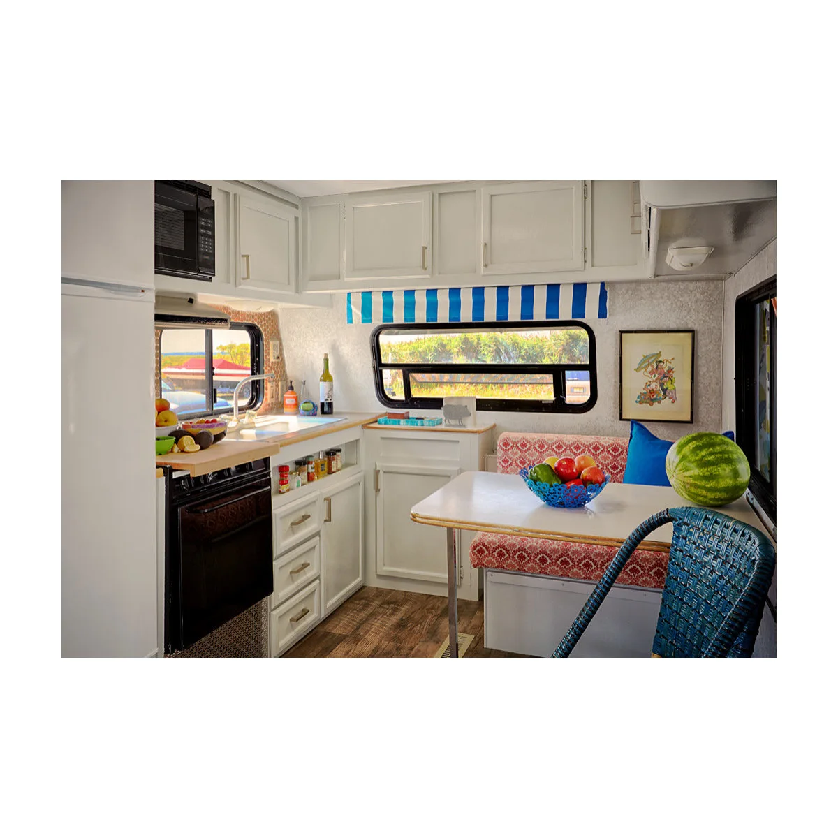 White camper kitchen and dinette with pink patterned cushions, a blue striped valance and a blue chair.