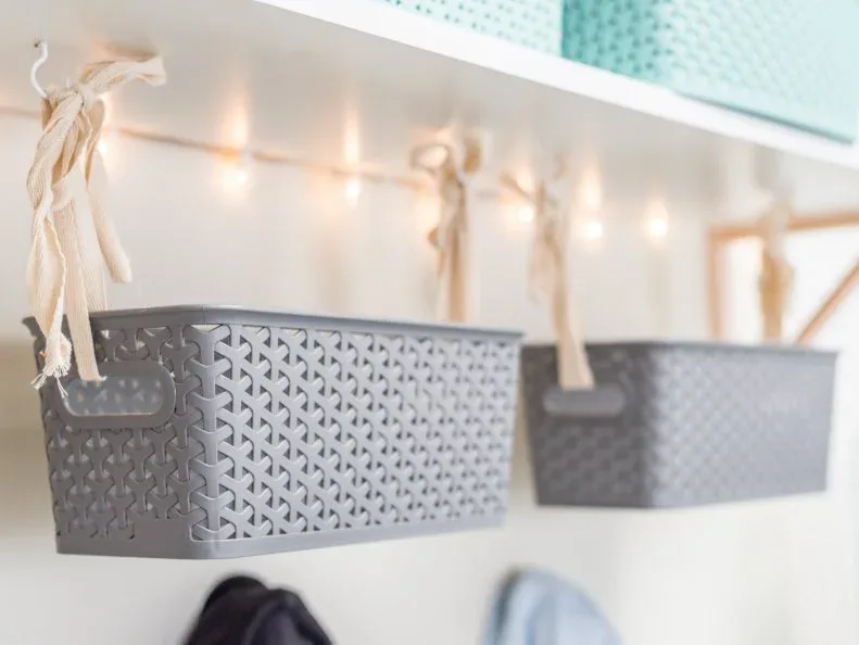 Small gray perforated baskets hanging beneath a white garage mudroom shelf.