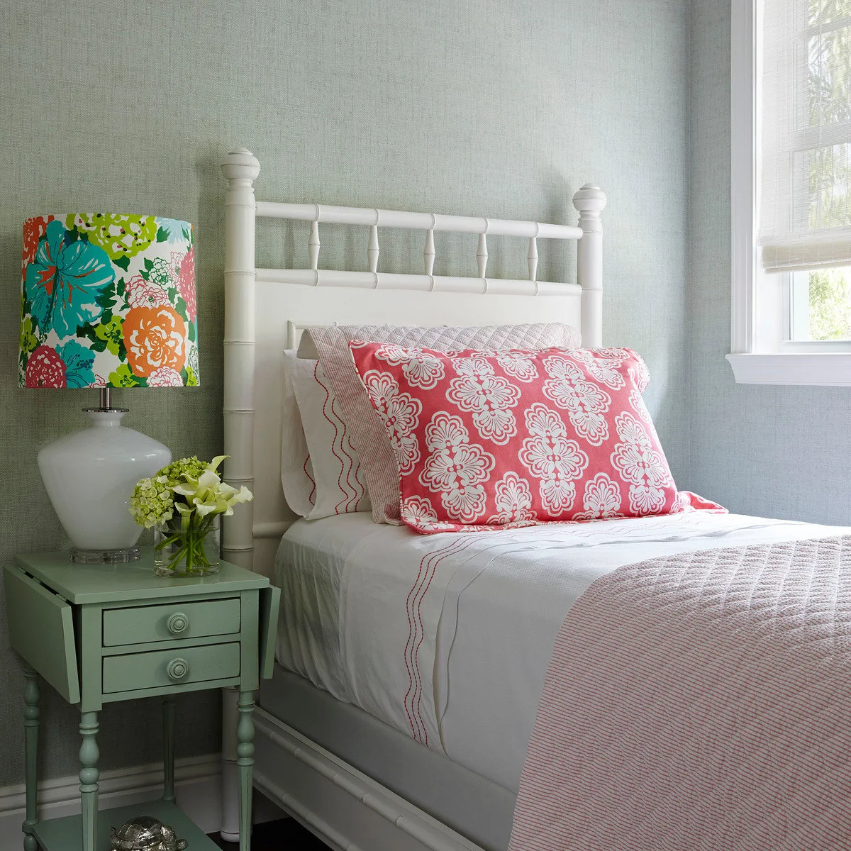 Mint-green nightstand with two drawers beside a white bed and colorful floral lamp shade