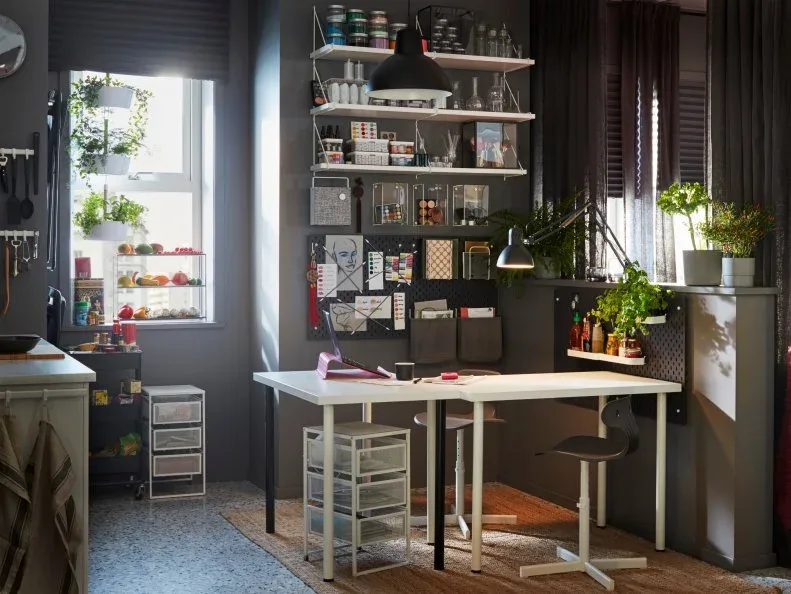 White project table with a task lamp, wall-mounted containers and shelves beside a kitchen counter