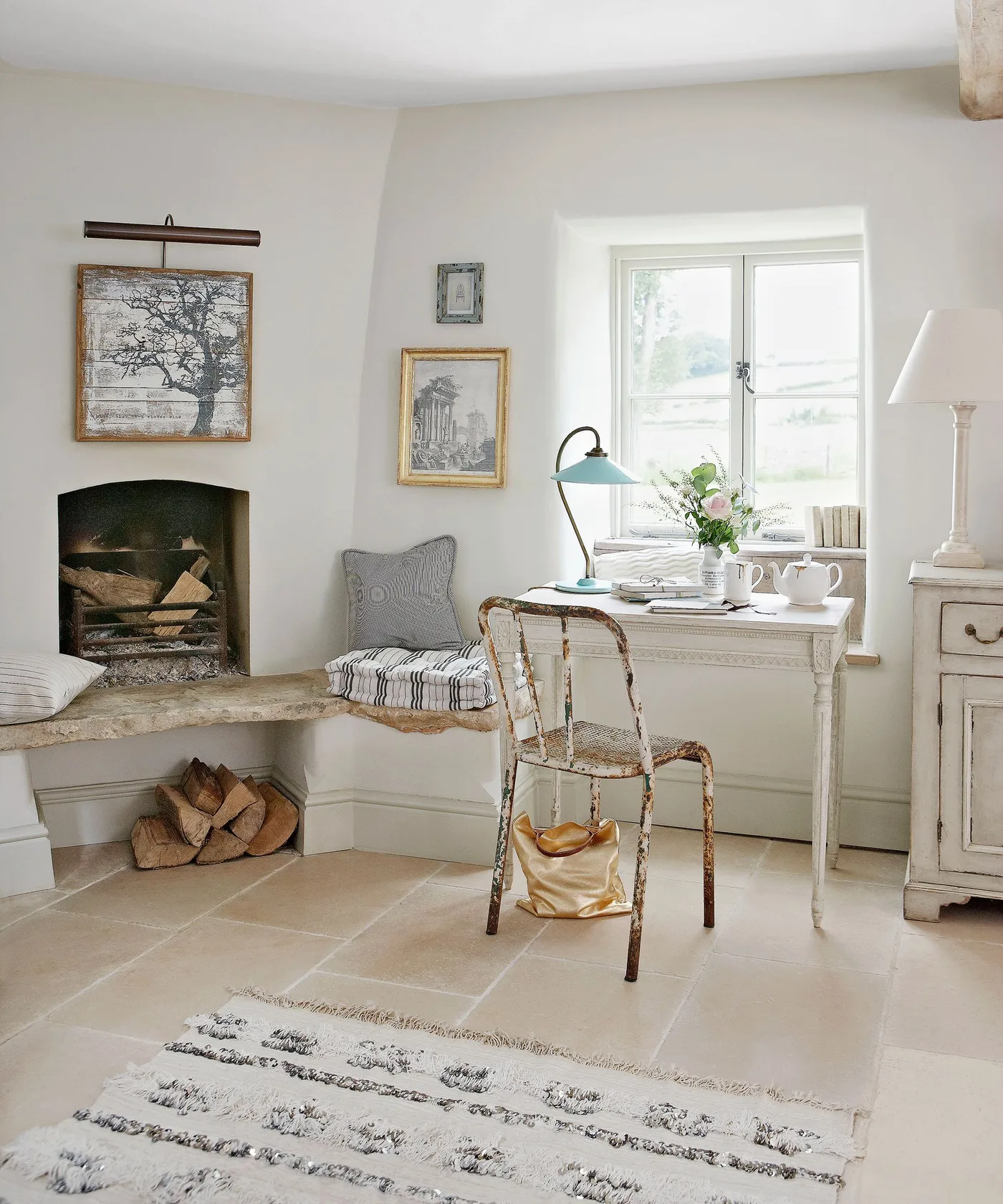 Pale arched fireplace with extended hearth bench, striped cushions, stored logs and nearby desk