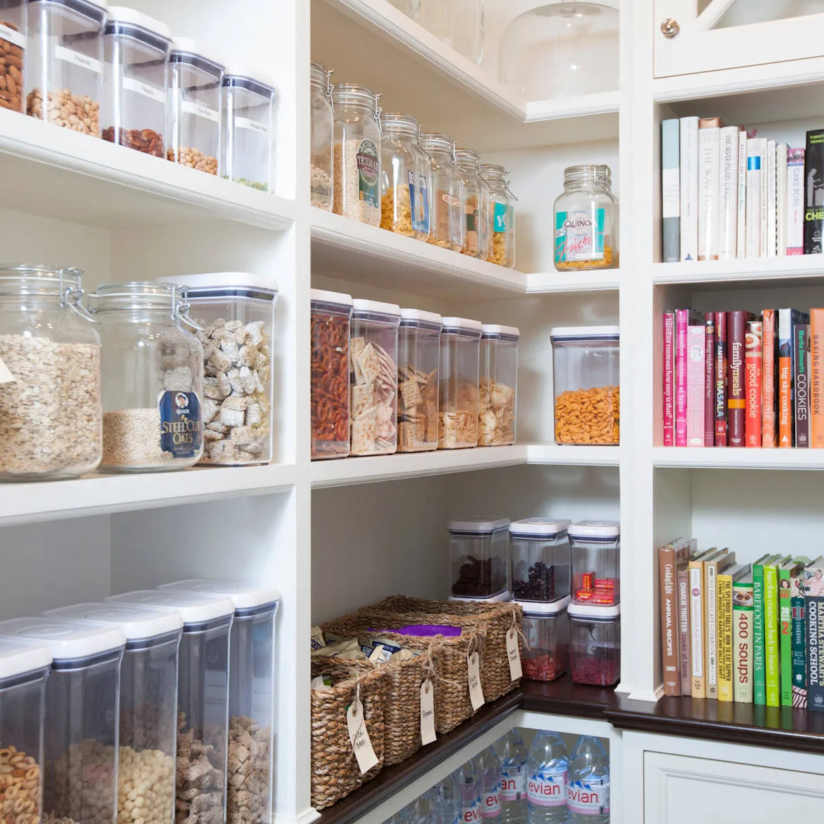 Clear food containers beside a column of cookbooks in a white corner pantry