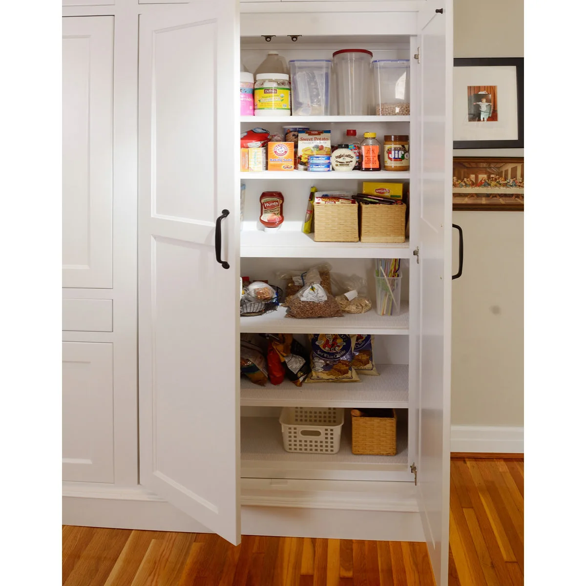 A tall white cupboard opens to show spaced food shelves with small baskets, containers and packets.