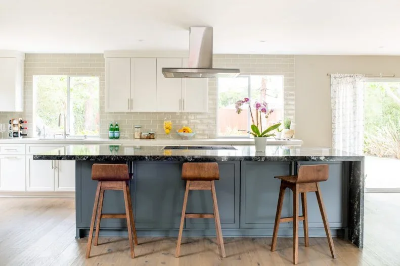 A dark island counter and gray cabinet fronts sit in front of white perimeter cabinets and pale rectangular backsplash tiles.