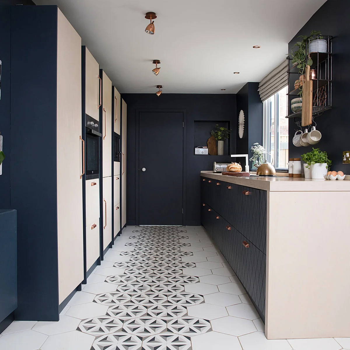 Terraced-house kitchen with dark walls, pale tall cabinet doors and a patterned central floor strip