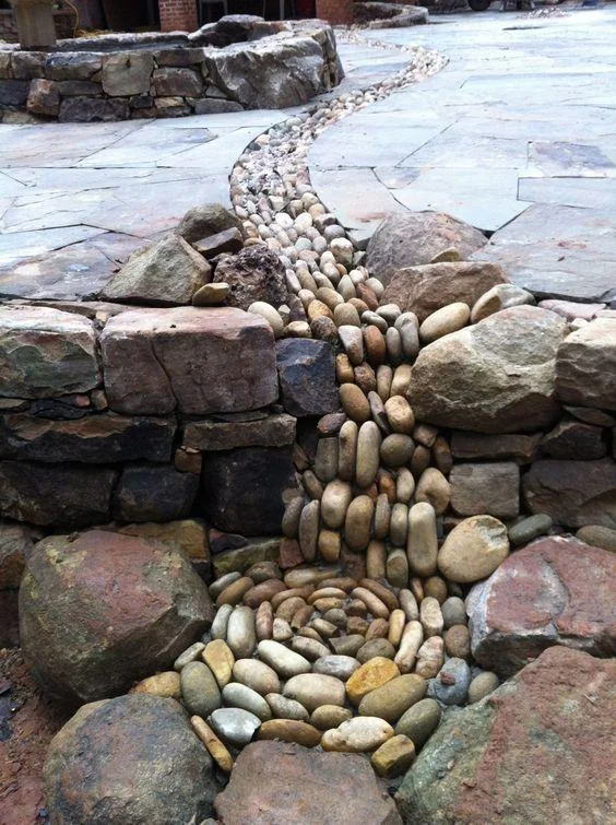 Upright rounded stones fill a narrow curving gap through gray paving and larger border rocks