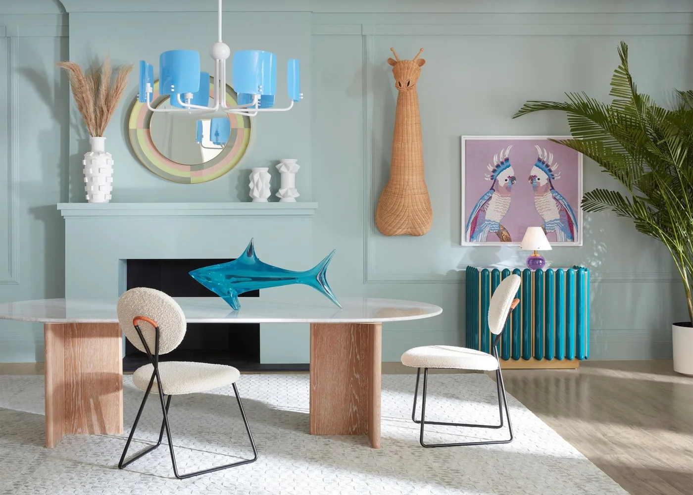Blue hanging light above a white oval dining table with wood supports in a pale green room