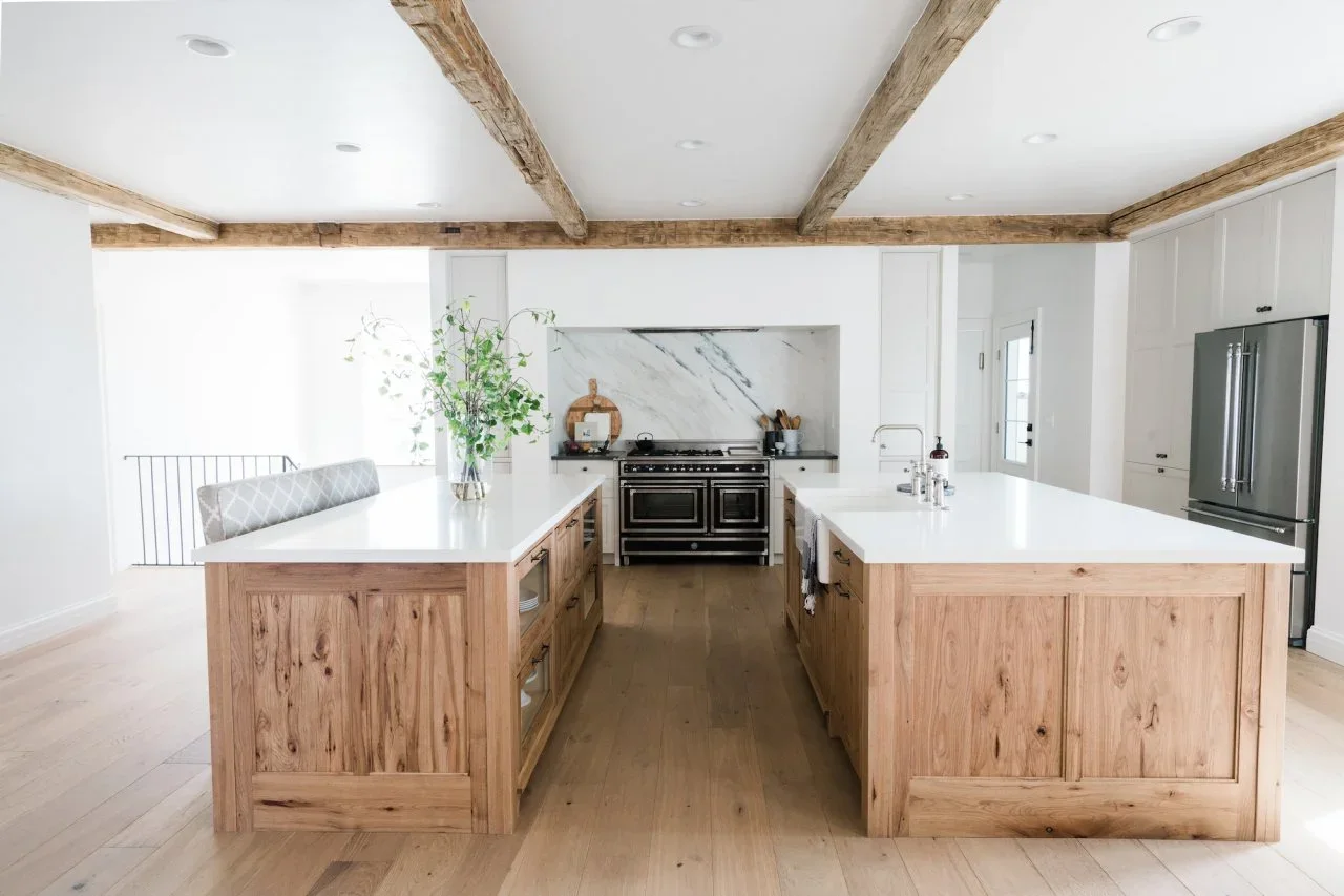Two knotty wood islands with pale tops stand opposite each other, one holding a sink and the other drawers and open shelves.