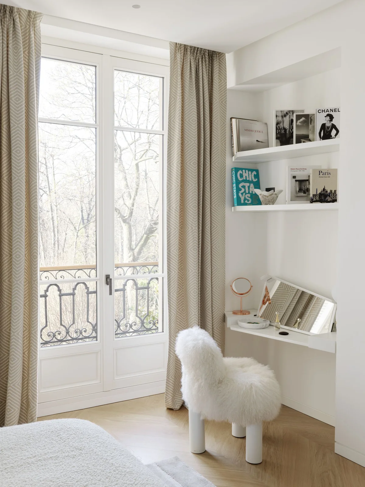 A white wall-mounted dressing surface with a rectangular mirror sits below display ledges beside tall windows