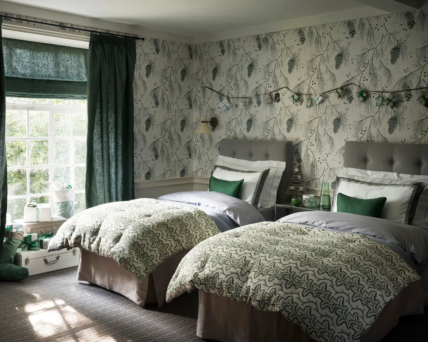 Twin bedroom with deep green curtains and blind, pale gray upholstered headboards, green cushions, patterned throws, and a central bedside table.
