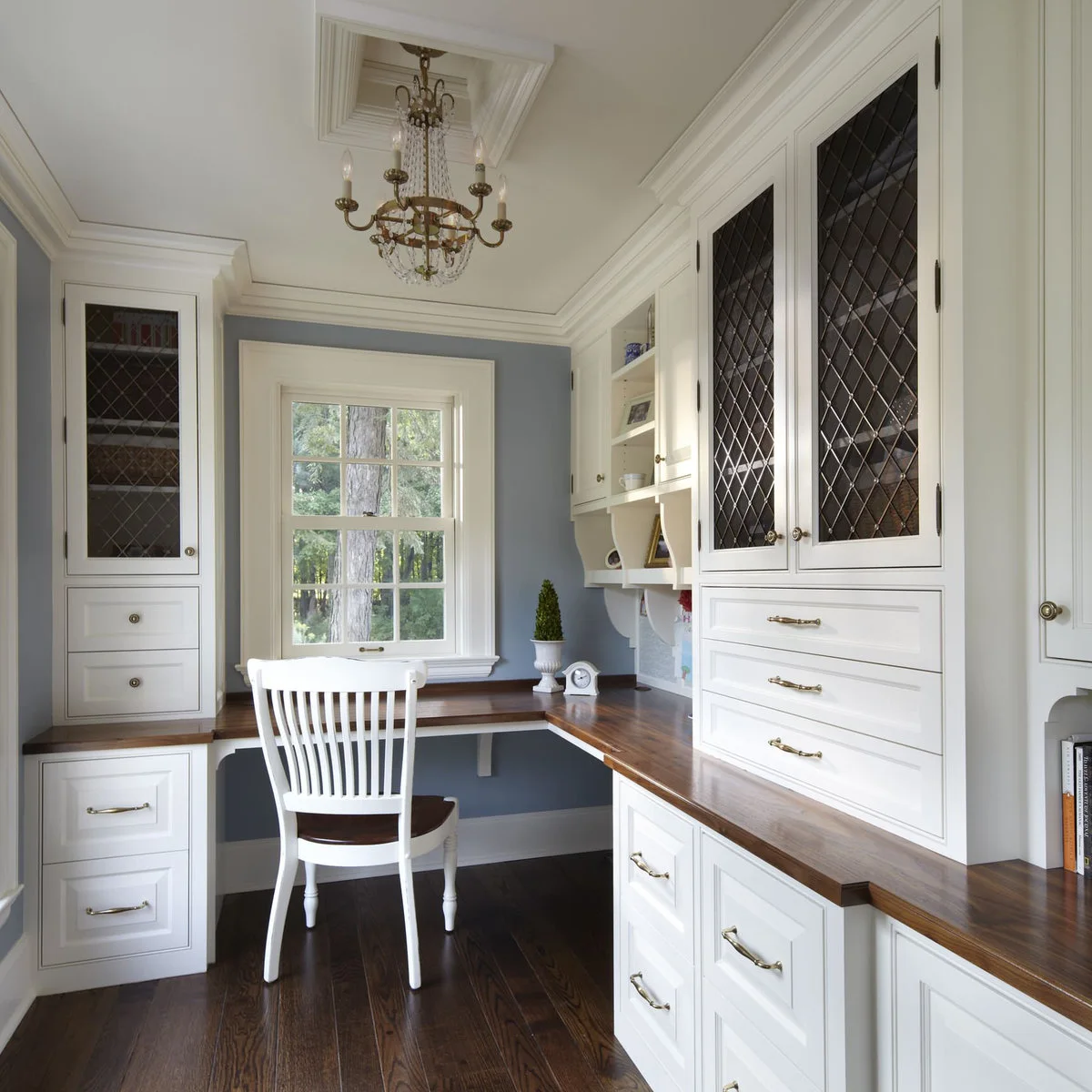 White home office cabinetry with wood counter, pale blue wall, glass-front upper cupboards and white chair