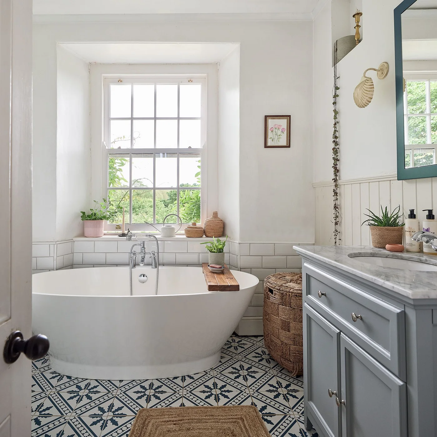 Lidded woven hamper between a freestanding bath and gray vanity