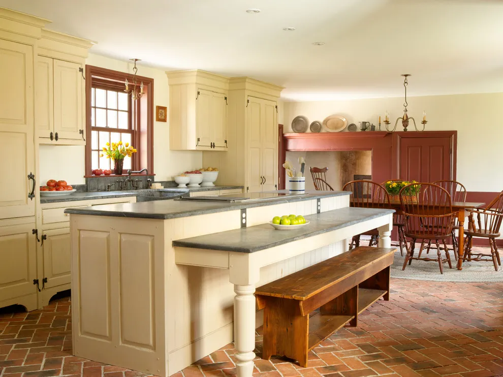 Cream cabinets and a pale island sit beside a wooden bench on a brick-patterned floor