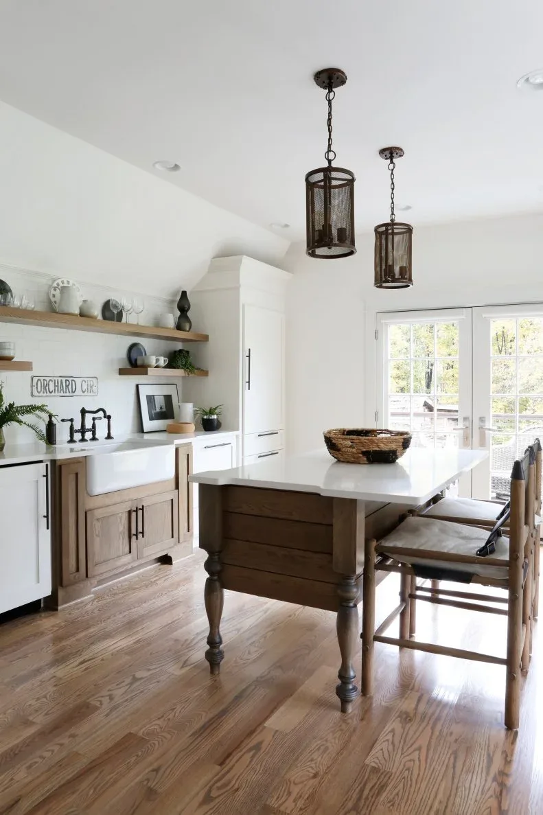 Pale country kitchen with turned-leg wood island, white top, tall wood chair, open shelves and dark lantern pendants