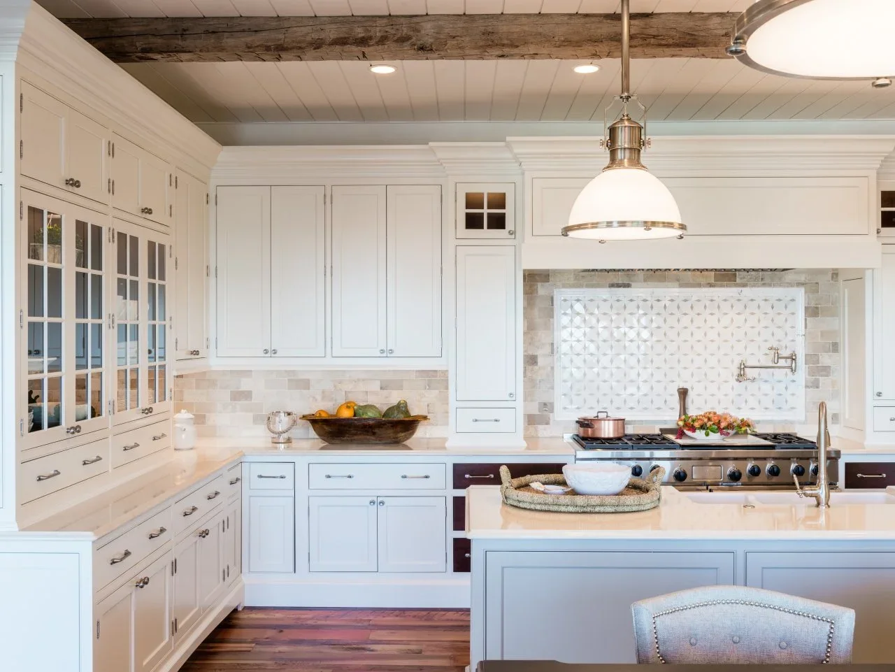 A pale country kitchen has a patterned white tile panel above the range framed by quieter rectangular tiles.