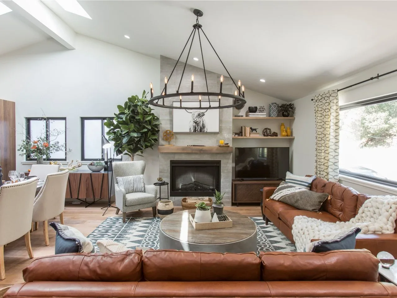 Tan leather sofas and a pale armchair gather around a round coffee table before a gray fireplace.