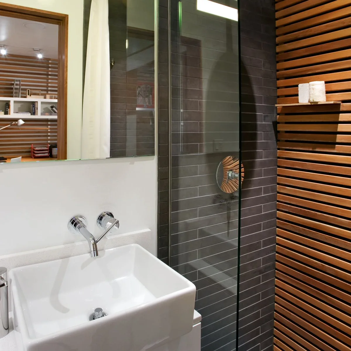 Dark tiled glass shower beside a horizontal timber screen and white basin