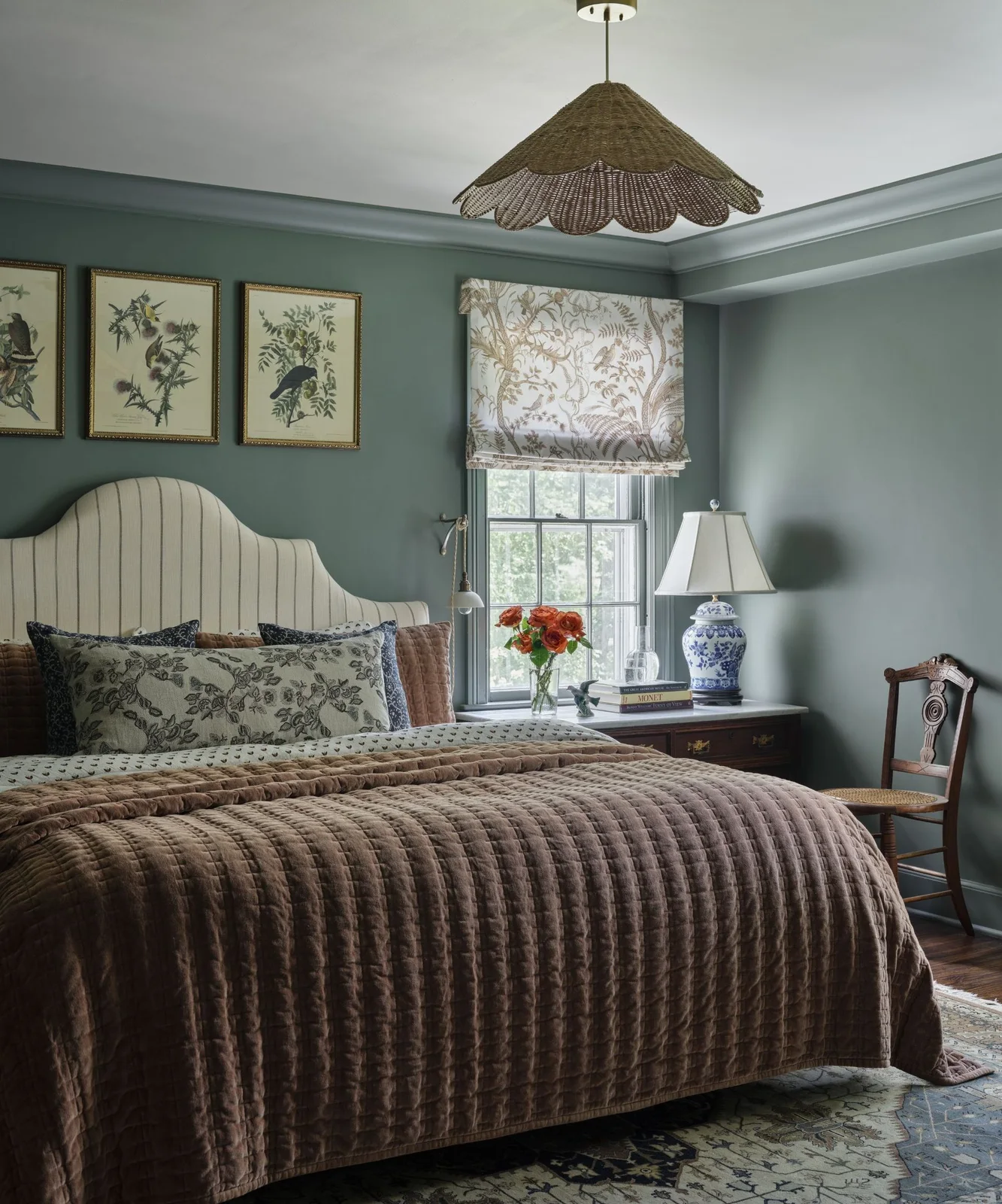 Muted blue-green bedroom walls with a striped headboard, brown quilt and pale patterned window blind.