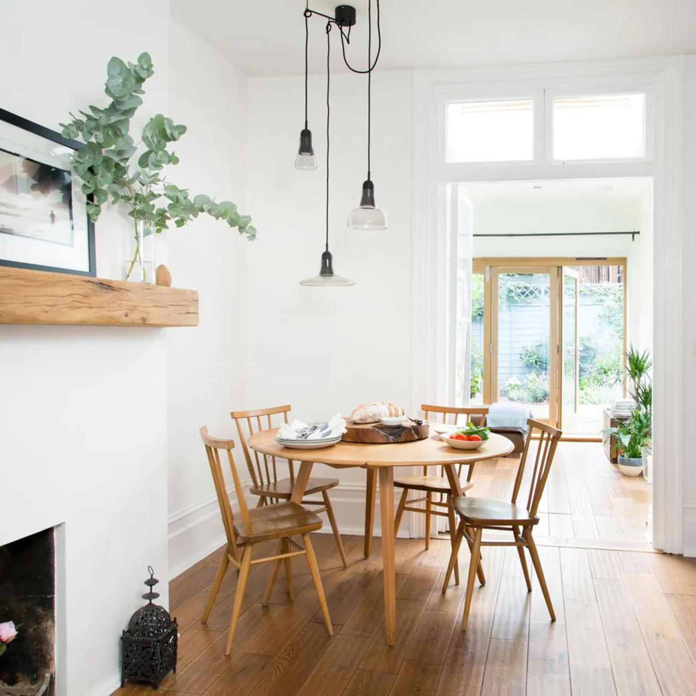 Three small clear shades at staggered heights above a round wood table beside a fireplace