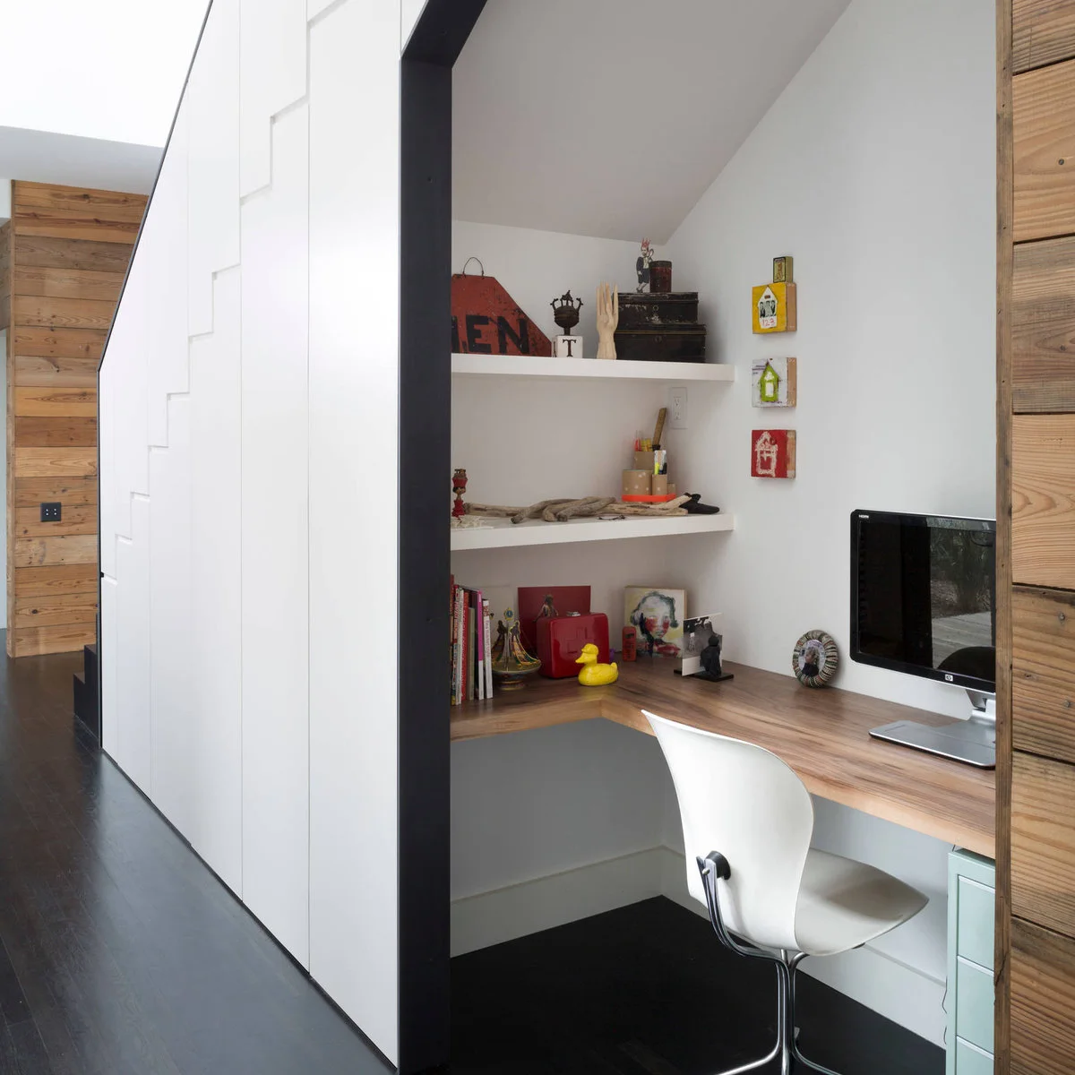 Under-stair desk with a wood L-shaped surface, white chair and two white shelves