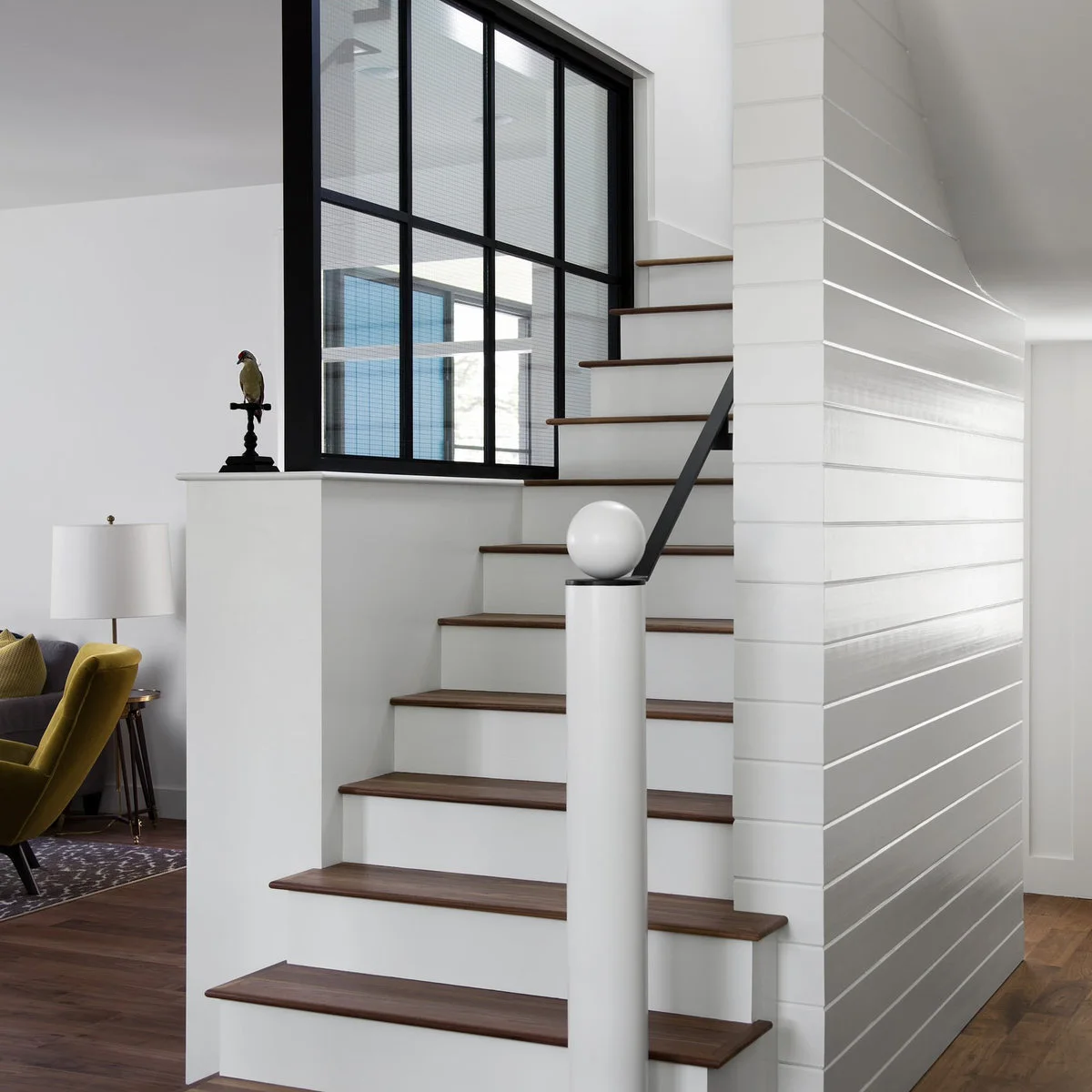 Horizontal white boards cover a narrow stair enclosure opposite black-framed interior glazing.