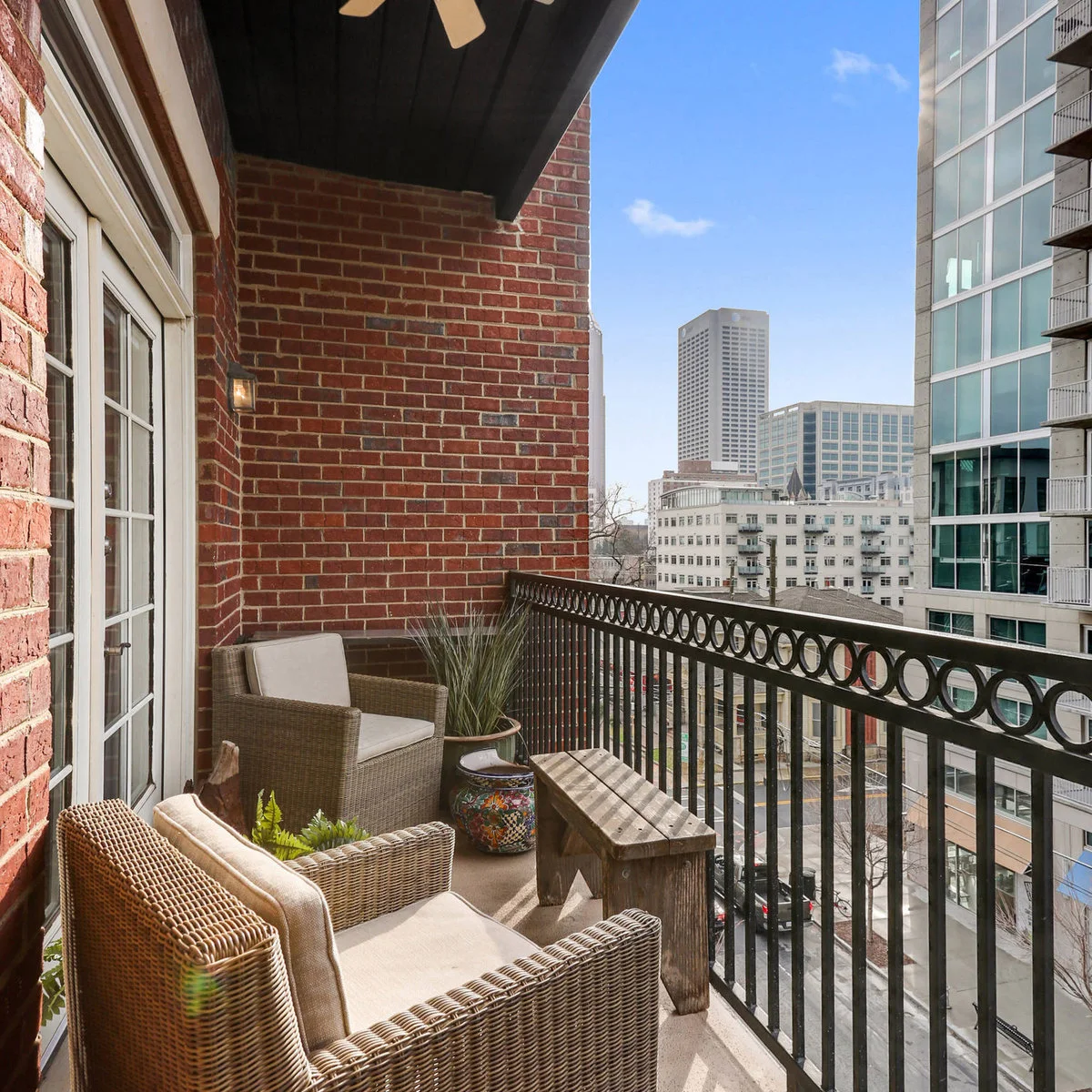 Two woven armchairs flank a narrow wooden table on a brick-walled balcony