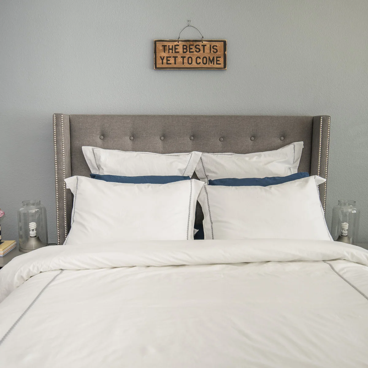 Simple teen bedroom with a gray upholstered headboard, white bedding and blue accent pillows