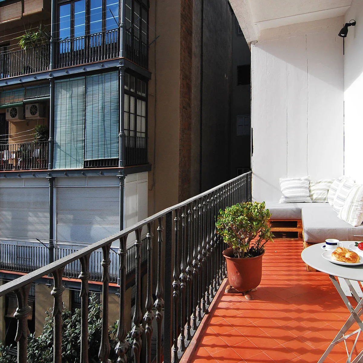 Long narrow balcony with pale cushioned end seating, orange floor tiles and a small folding table