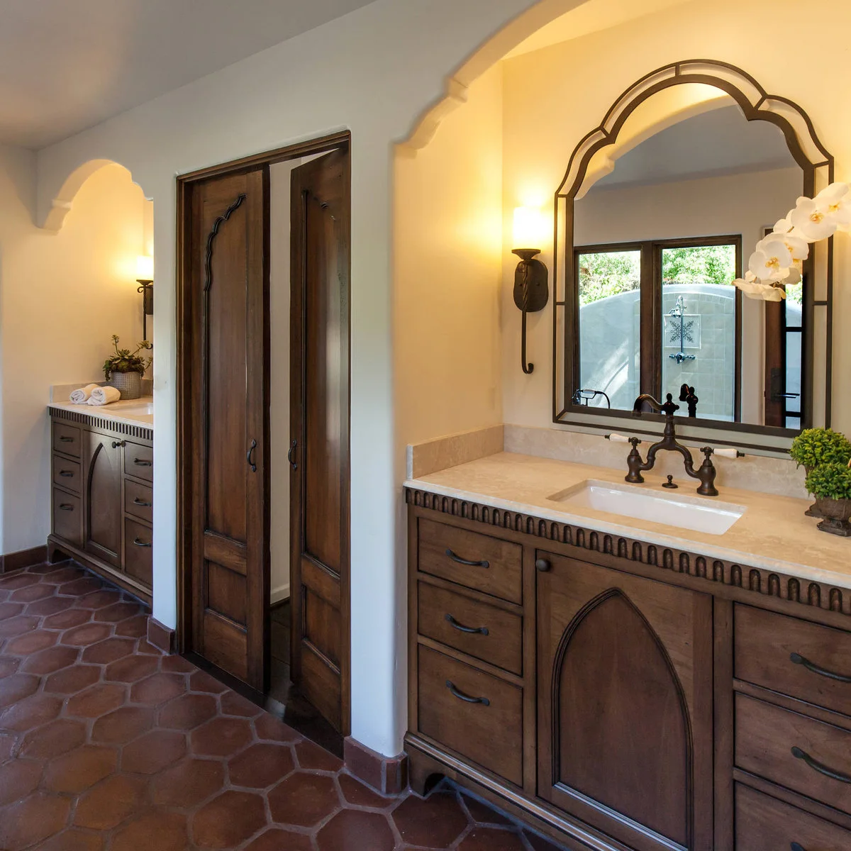 Bathroom with terracotta-colored hexagonal floor tiles, dark wood vanities and arched mirror recesses