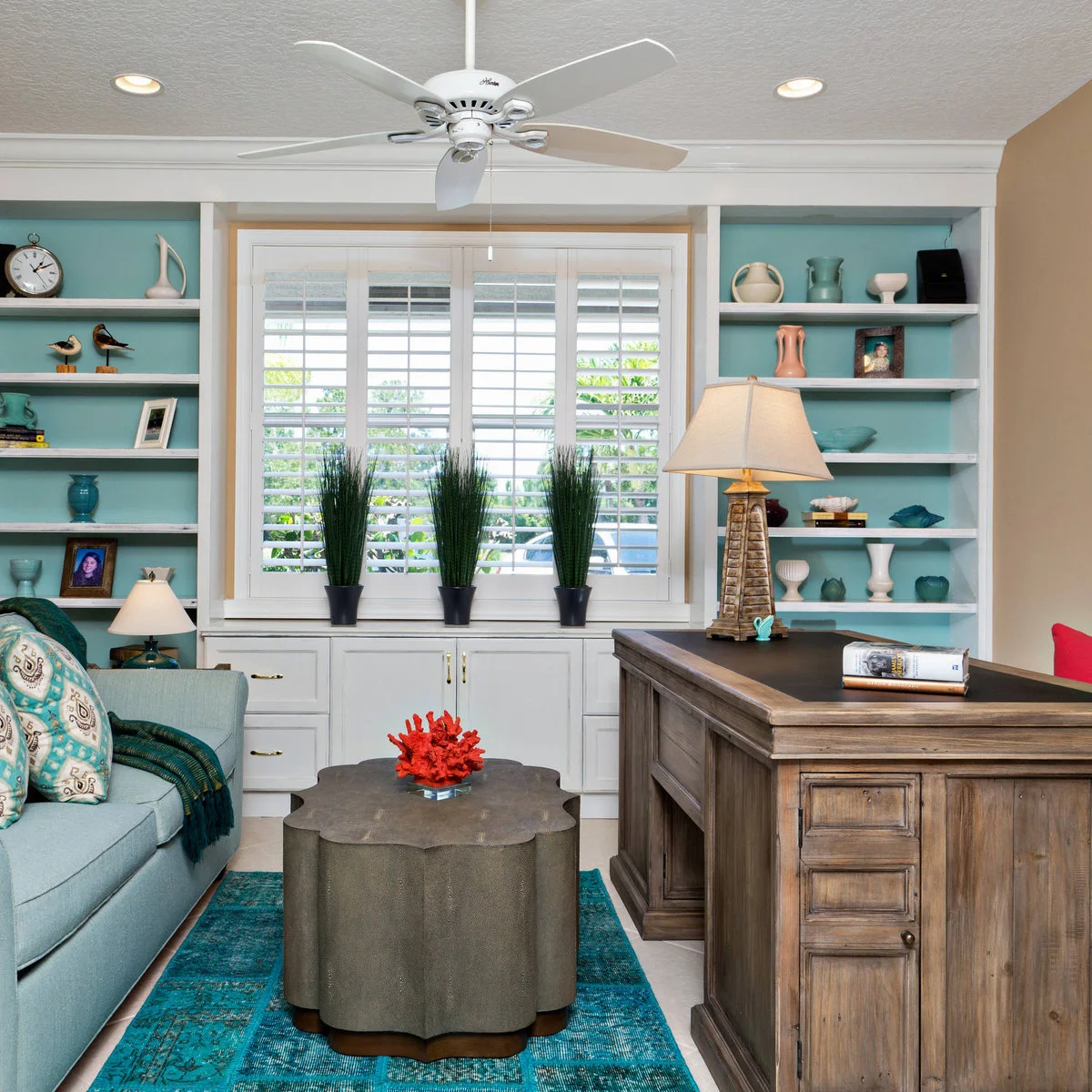 A wood desk beside a pale blue sofa, with blue-backed shelves, small ceramics and a low shaped table.