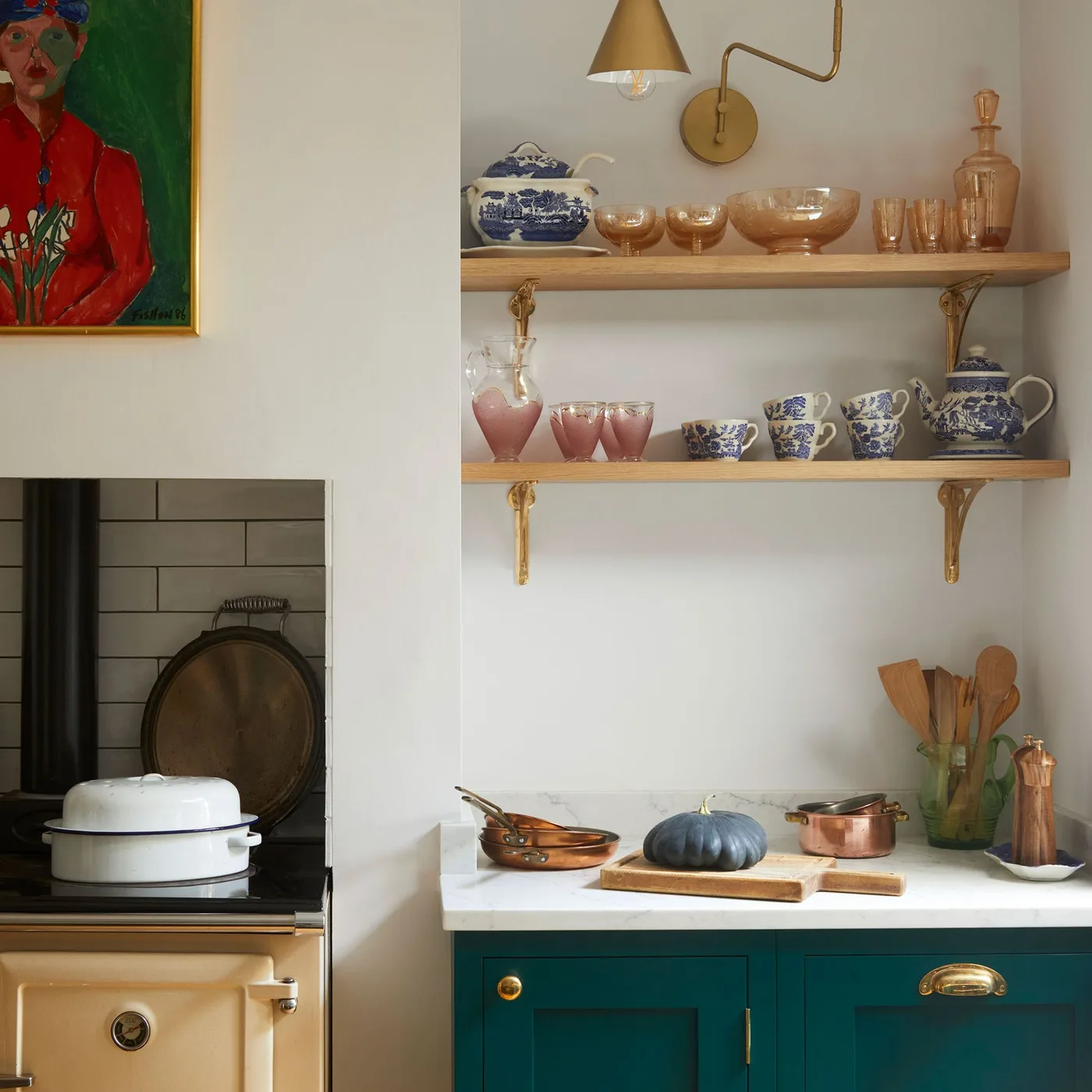 Kitchen detail with green paneled cabinets, gold-colored handles, pale wall, wooden shelves and a cream-colored range.