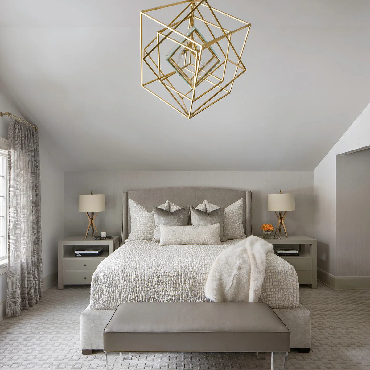 A bed under a sloping ceiling with matching nightstands that combine open book shelves and drawers, plus two shaded lamps.