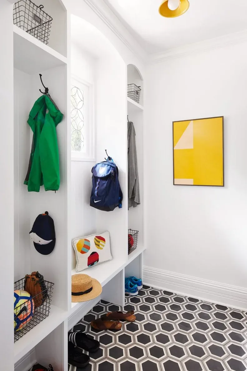 A short white bench sits beneath a window between tall storage bays with wire baskets, above a black-and-white hexagonal floor.